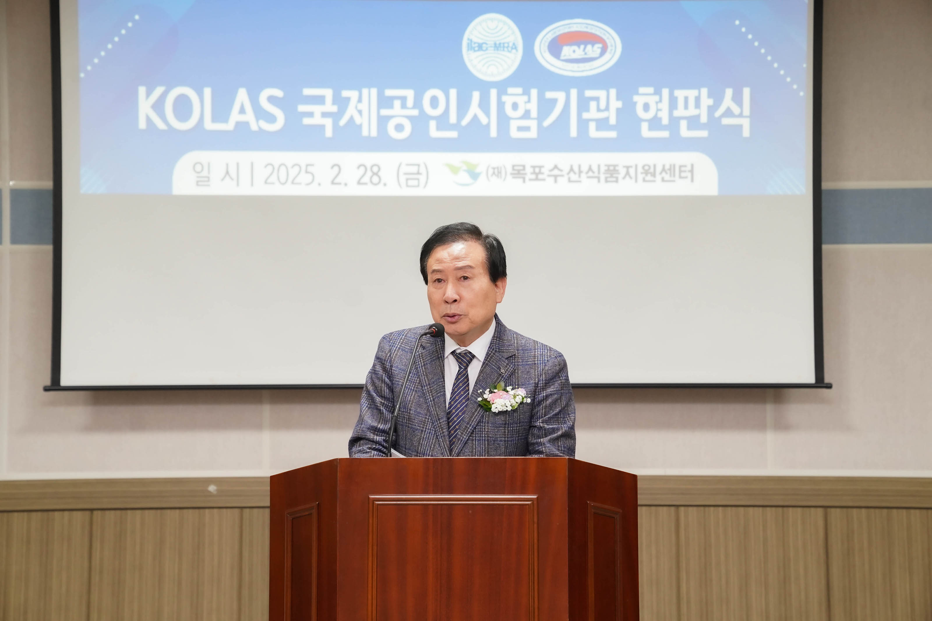 박홍률 목포시장이 연단에서 마이크를 들고 발언하는 장면. 뒤에는 스크린에 다음과 같은 텍스트가 보임
'제목: KOLAS 국제공인시험기관 현판'
'하단 텍스트: 일 시 | 2025. 2. 28. (금) / (재)목포수산식품지원센터'