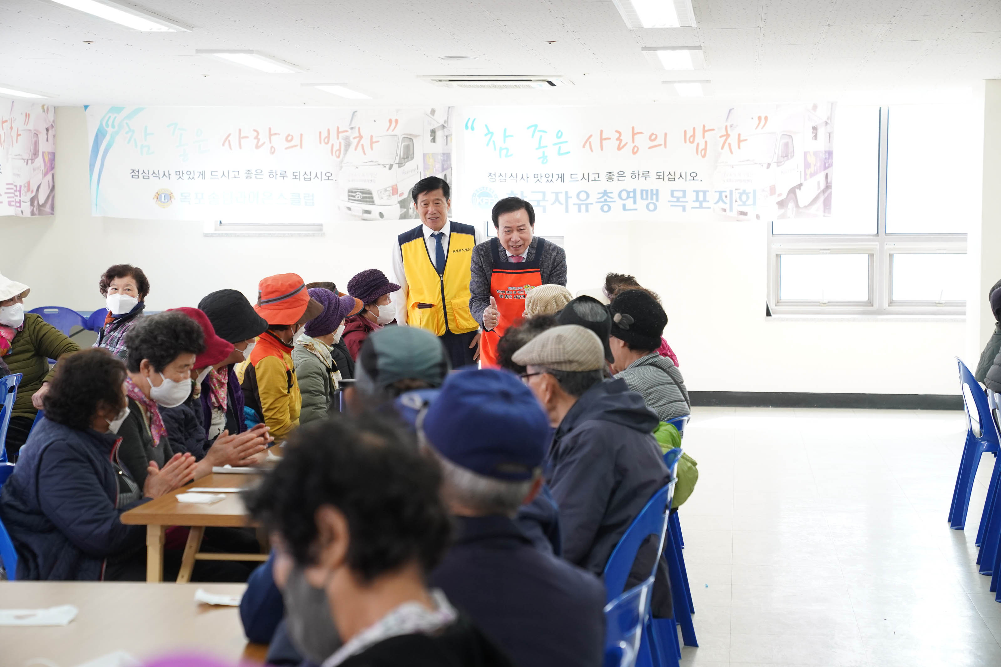 어르신들이 않아있는 식탁에서 주황 앞치마를 입고 얘기를 하고 있는 박홍렬 목포시장의 모습