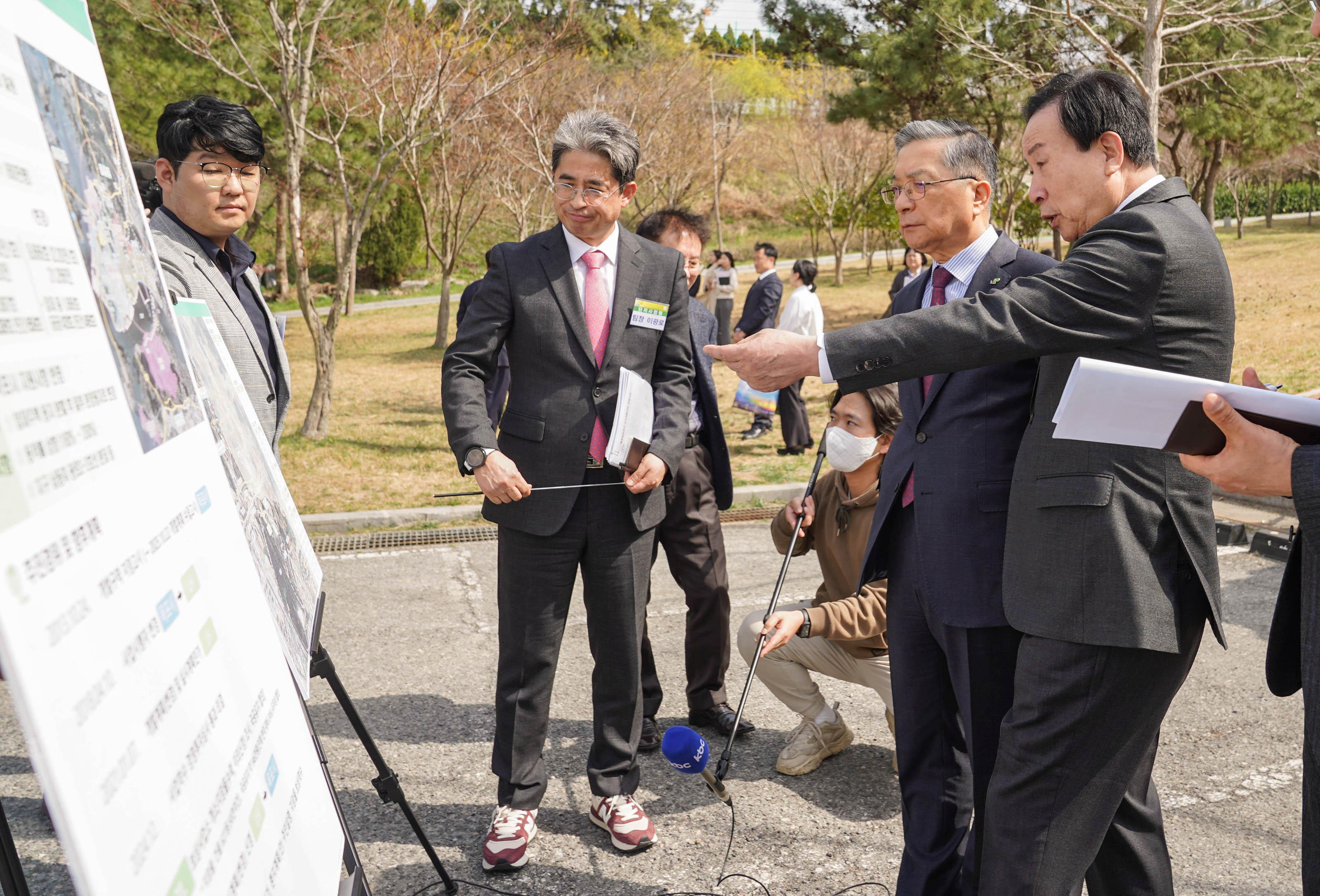 야외 브리핑 현장에서 양복을 입은 박홍률 목포시장과 이한준 한국주택토지공사 사장이 화이트보드를 보며 토의하고 있다. 박홍률 목포시장은 손가락으로 어떤 부분을 지적하고 있는 모습