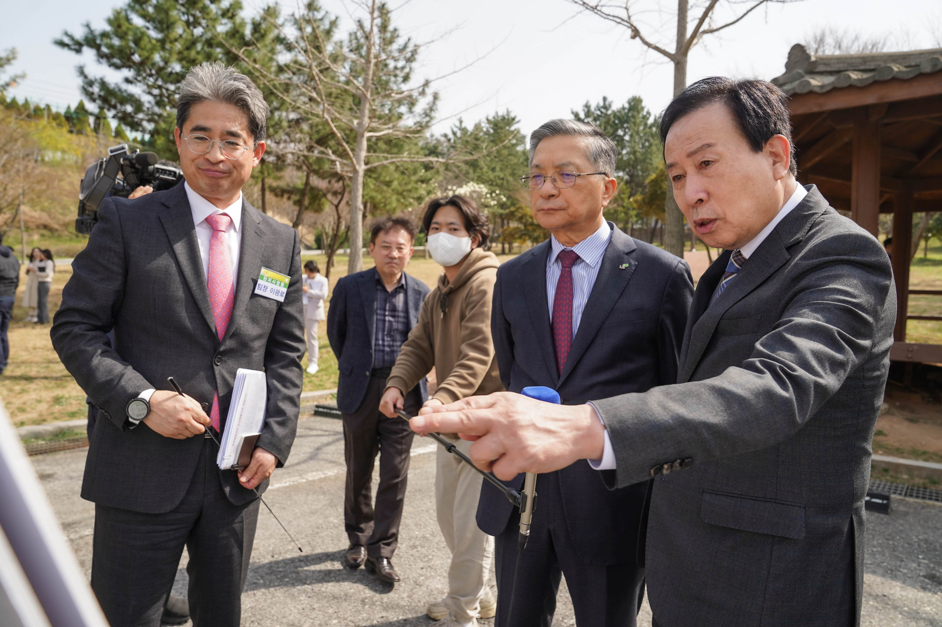 양복 차림의 박홍률 목포시장과 이한준 한국주택토지공사 사장이 화이트보드를 보며 토의 중이다. 뒤에는 취재진이 있고 나무와 정자가 있는 공원에서 촬영중인 모습
