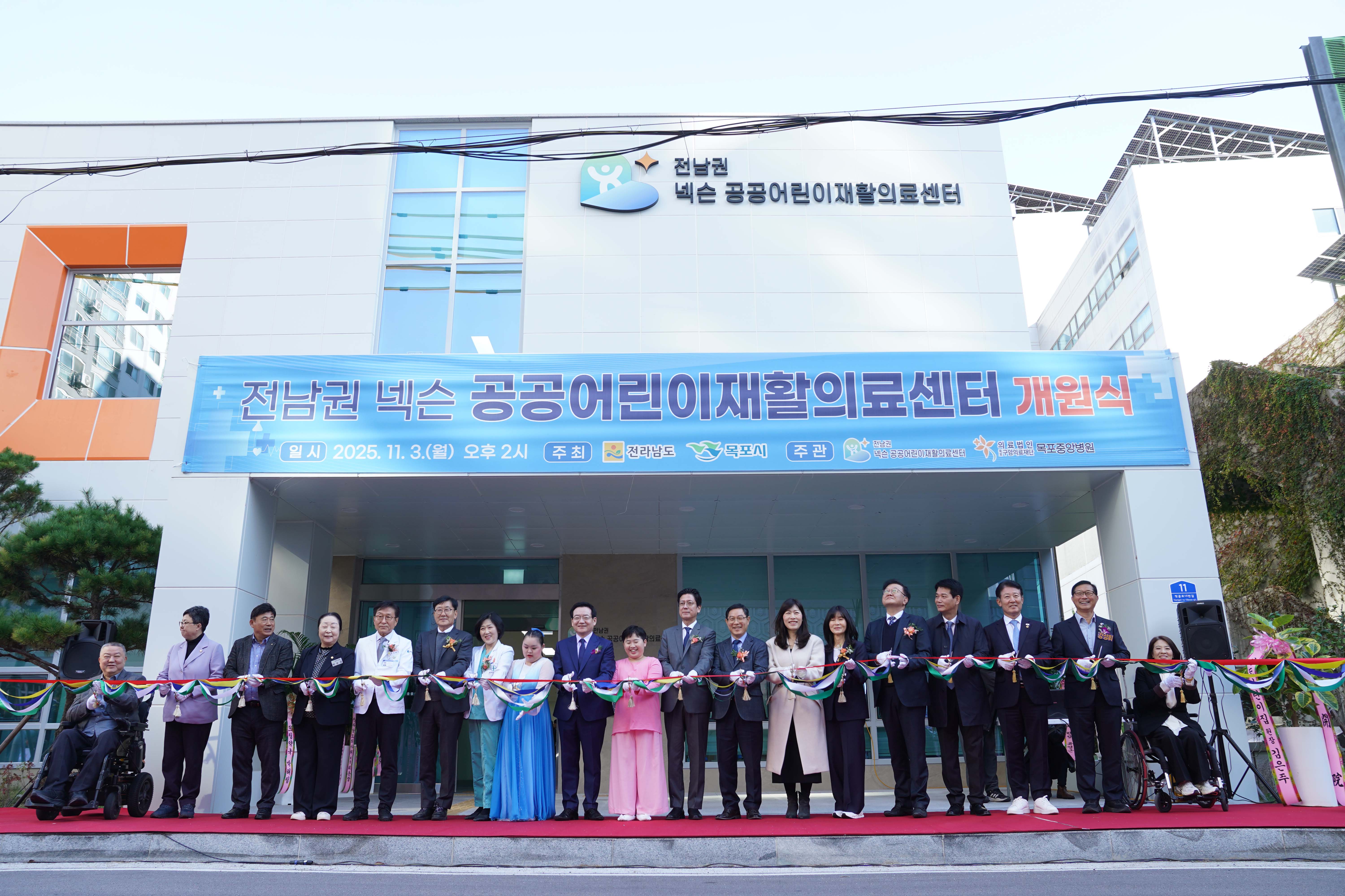 센터 건물 입구에서 진행된 테이프 커팅식. '전남권 넥슨 공공어린이재활의료센터 개원식 (2025. 11. 3. 월요일)' 현수막이 걸려 있고, 내빈들이 나란히 서서 테이프를 자르고 있음.