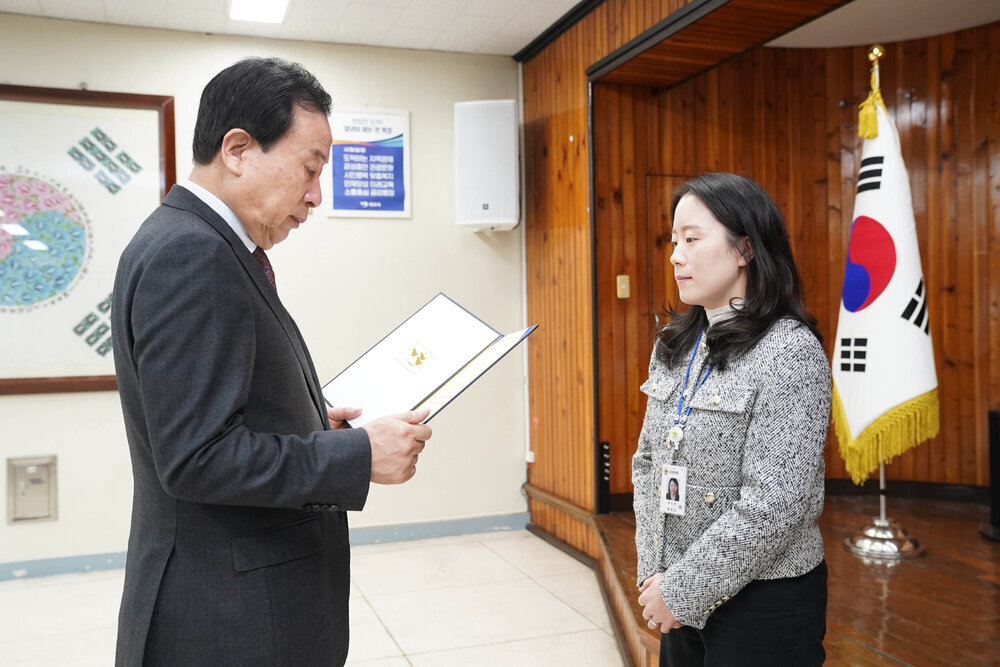 3월 정례조회에서 정장을 입은 남성이 회색 재킷을 입은 여성에게 표창장을 전달하는 모습