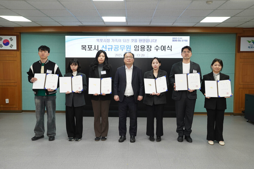 신규자 임용식에서 임용장을 받은 직원들과 정장을 입은 남성이 함께 임용장을 들고 기념촬영을 하는 모습