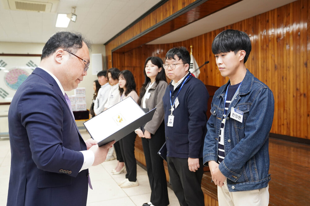 정장을 입고 안경을 낀 남성이 청자켓을 입은 천의현에게 상장을 수여하고 있다