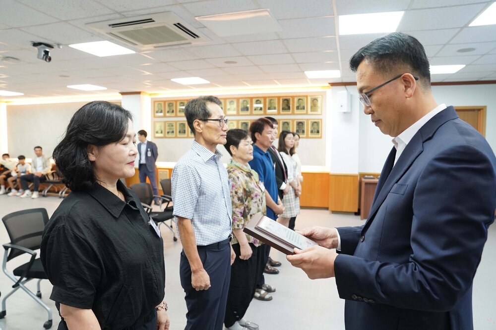 정장 차림의 관계자가 단정한 복장의 시민에게 표창패를 전달하고 있는 모습이다.