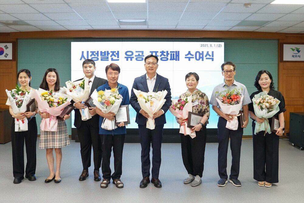 ‘시정발전 유공 표창패 수여식’에서 정장과 단정한 복장의 수상자들이 꽃다발과 표창패를 들고 단체 기념 촬영을 하고 있는 모습이다.