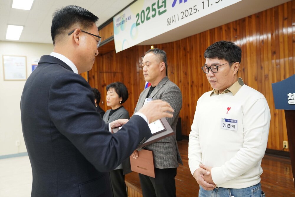 11월 정례조회로 정장을 입고 안경을 쓴 남성이 안경을 쓰고 흰색 니트를 입고 두손을 가지런이 모은 장준혁 수상자에게 상패를 수여 하고 있다.