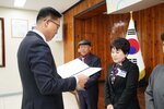 11월 정례조회로 정장을 입고 안경을 쓴 남성이 짧은 머리에 보라색블라우스를 입고 검은 정장을 입은 김정단 수상자에게 상장을 수여 하고 있다.