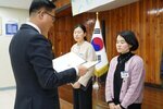 11월 정례조회로 정장을 입고 안경을 쓴 남성이 검은색 티에 연보라색 가디건을 입은 유경화 수상자에게 상장을 수여 하고 있다.